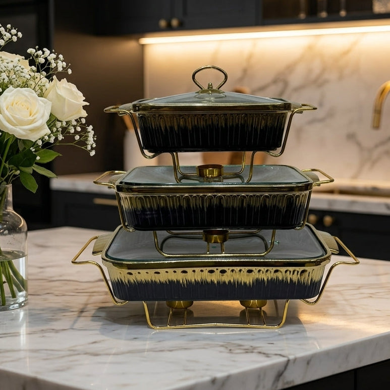 Stacked 3-piece luxury ceramic chafing dish set in black and gold with glass lids on a marble countertop.