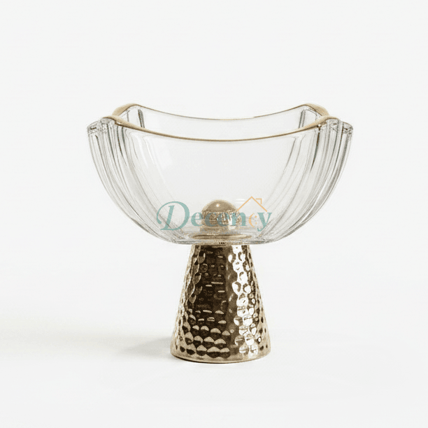 Luxury clear crystal fruit bowl with a gold rim placed on a hammered metal pedestal stand on a marble kitchen island.