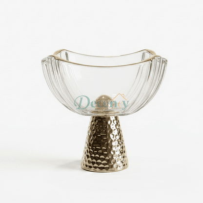 Luxury clear crystal fruit bowl with a gold rim placed on a hammered metal pedestal stand on a marble kitchen island.