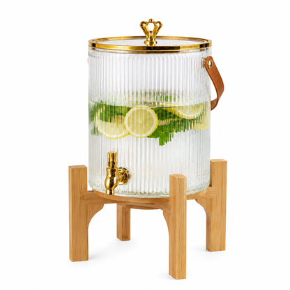 Luxury 5.5L glass drink dispenser with a gold tap and solid wooden stand displayed on a white marble table.