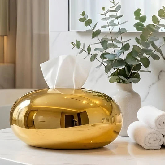 Modern gold oval tissue box cover with metallic finish placed on a marble tabletop.