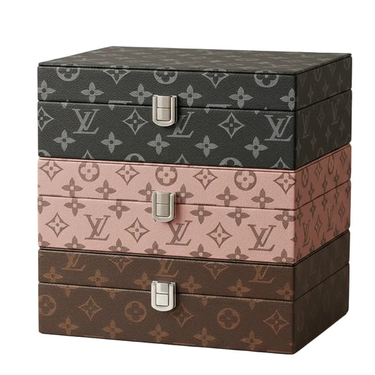 Stack of three luxury LV design leather jewellery boxes in black, dusty pink, and brown on a vanity table.