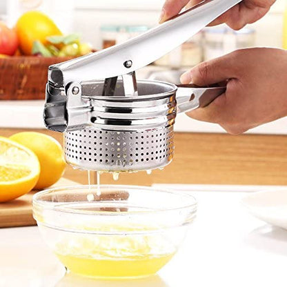Stainless steel manual potato presser pressing half an orange in a kitchen setting