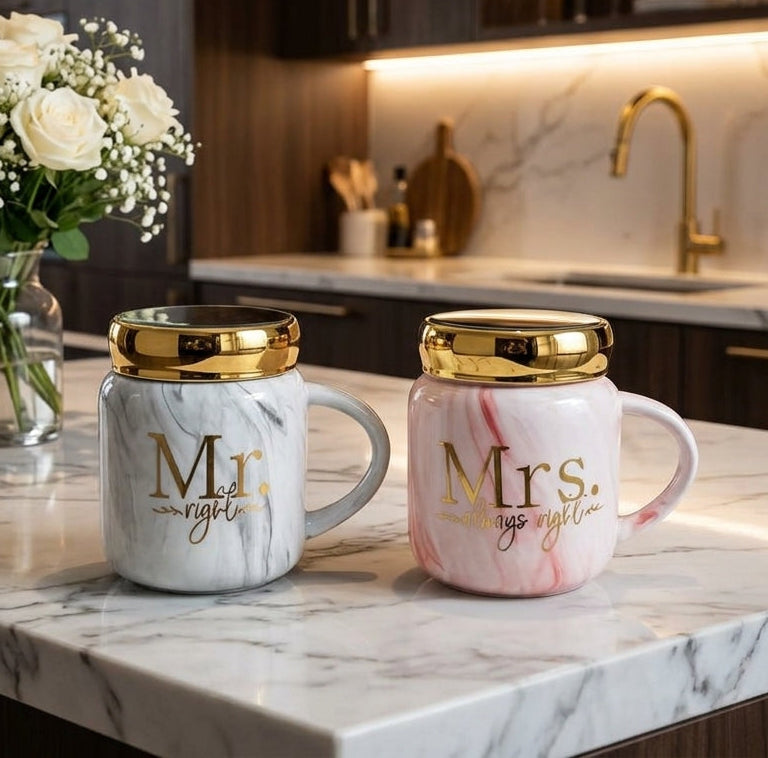 Pair of grey and pink marble Mr and Mrs ceramic coffee mugs with gold metallic lids placed on a marble kitchen counter.
