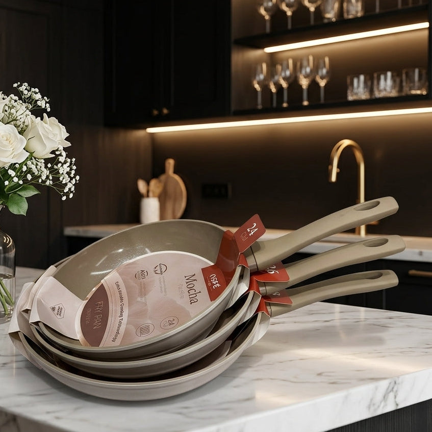 Stack of OSFE Mocha non-stick ceramic frypans on a marble kitchen countertop.