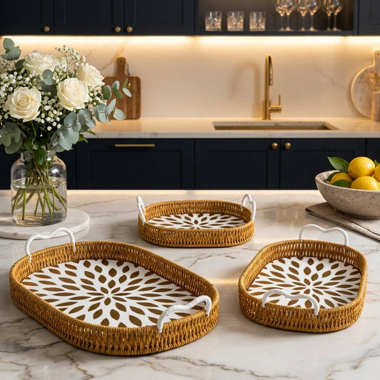 Set of three oval woven rattan serving trays with white handles displayed on a marble kitchen counter.