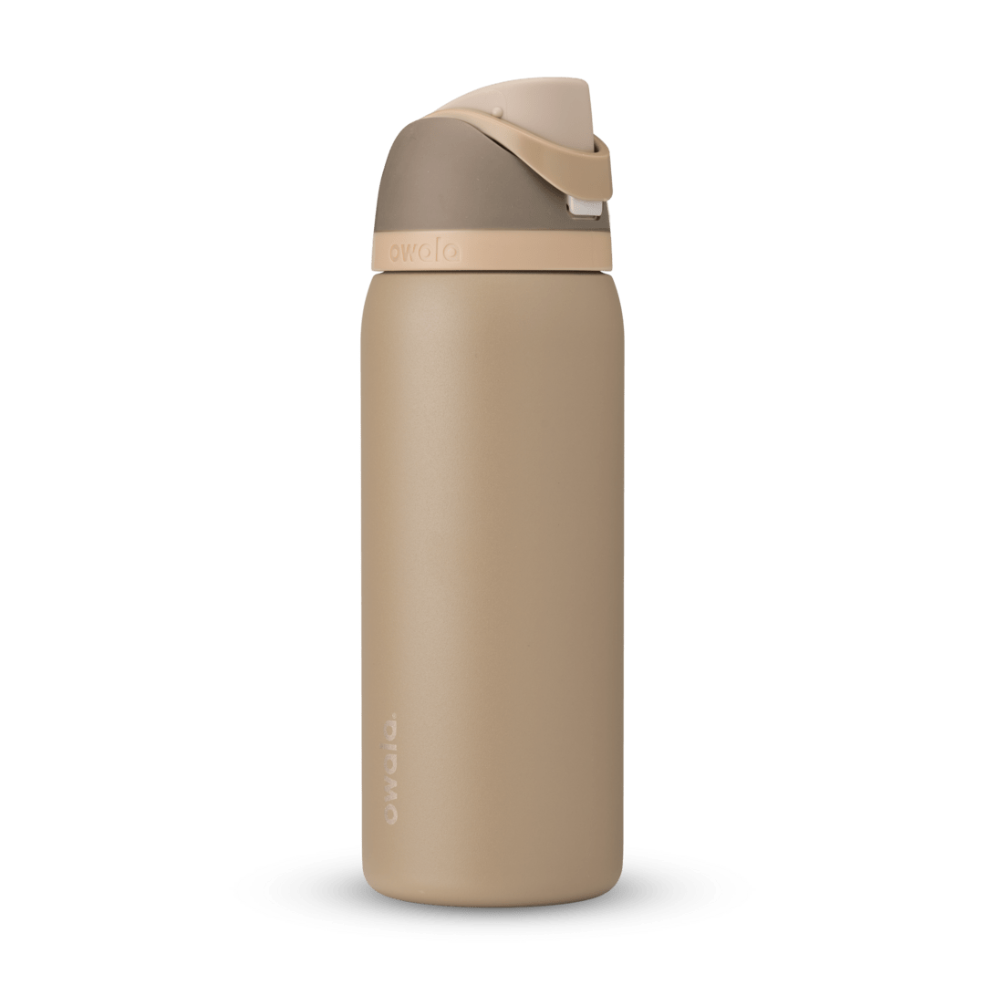 Owala FreeSip 32 oz insulated water bottle in desert tan and brown standing upright on a white marble kitchen countertop.
