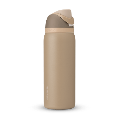 Owala FreeSip 32 oz insulated water bottle in desert tan and brown standing upright on a white marble kitchen countertop.