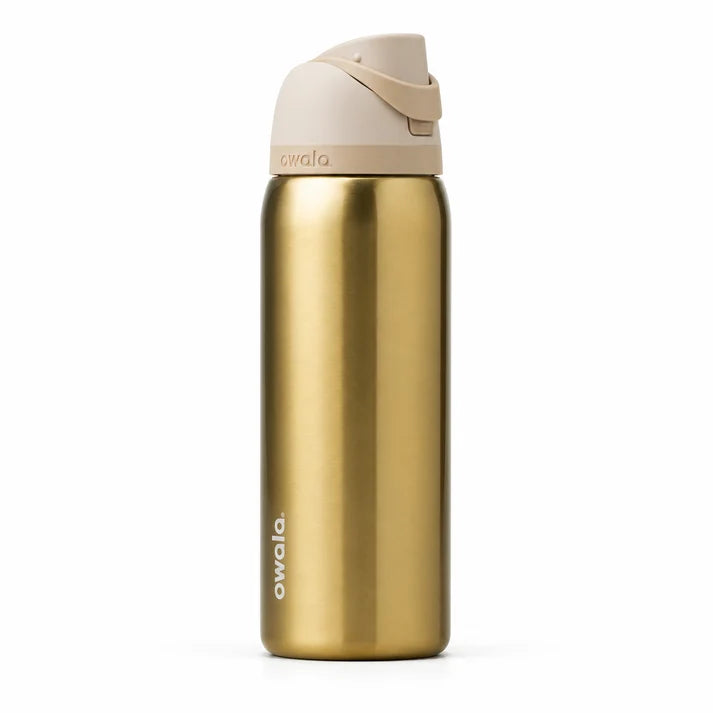 Owala FreeSip 32 oz stainless steel water bottle in Golden Tune shade sitting on a marble kitchen counter.