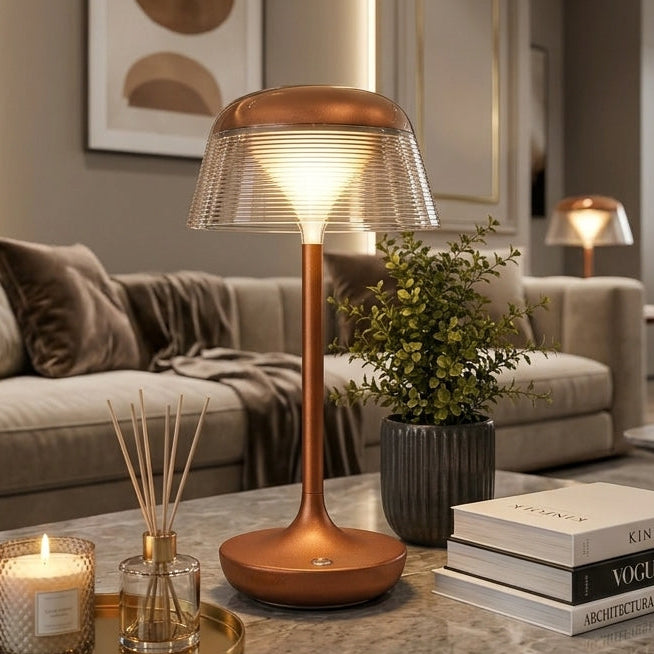 Modern rechargeable LED table lamp with a ribbed amber glass shade and metallic copper base placed on a wooden study desk.