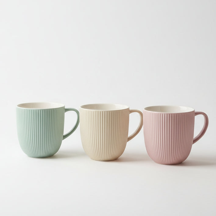Set of three ribbed ceramic tea mugs in pastel green, beige, and pink displayed on a kitchen counter.