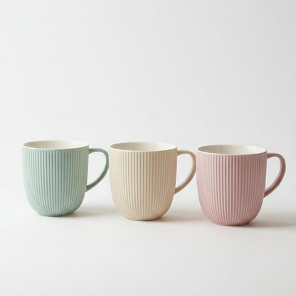 Set of three ribbed ceramic tea mugs in pastel green, beige, and pink displayed on a kitchen counter.
