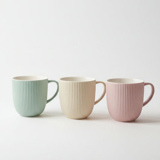 Set of three ribbed ceramic tea mugs in pastel green, beige, and pink displayed on a kitchen counter.