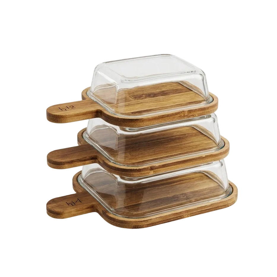 Stack of three square glass serving dishes with wooden lid handles on a kitchen counter