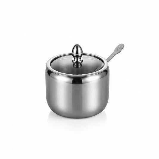 Stainless steel sugar jar container with a clear glass lid and small serving spoon on a marble countertop