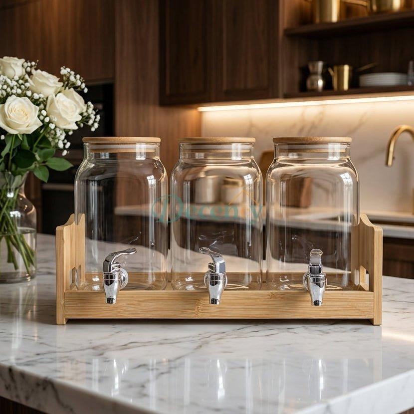 Triple glass beverage dispenser set with natural wooden lids and stand on a kitchen counter.