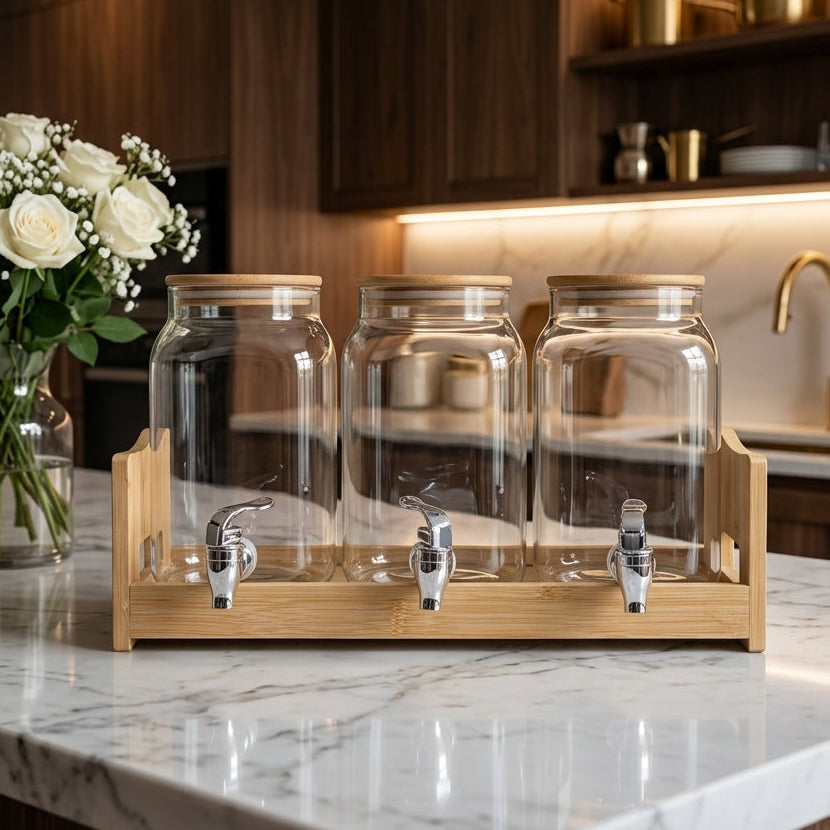 Triple glass beverage dispenser set with natural wooden lids and stand on a kitchen counter.