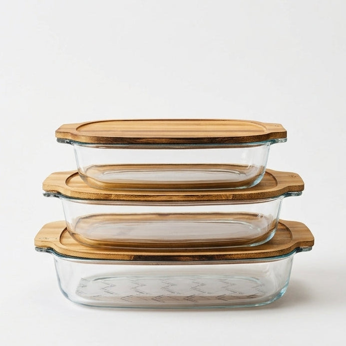 A stacked 3-piece set of clear glass serving dishes with natural wooden lids sitting on a marble kitchen island counter