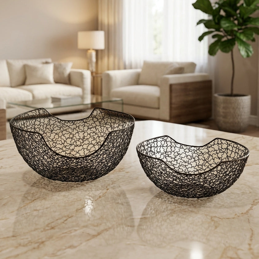 Set of two black wavy wire mesh fruit bowls displayed on a marble tabletop in a living room setting
