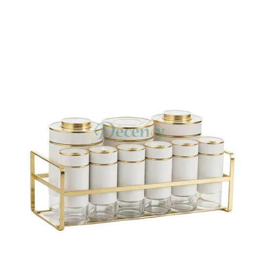Luxury white spice containers with gold-rimmed caps organized on a gold metal stand set on a marble kitchen counter.