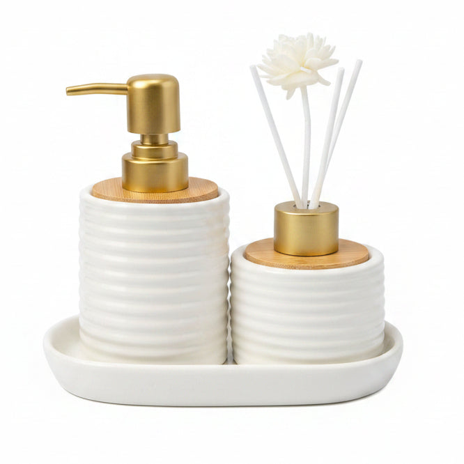 White ribbed ceramic soap dispenser and reed diffuser with flower sticks sitting on a ceramic tray.